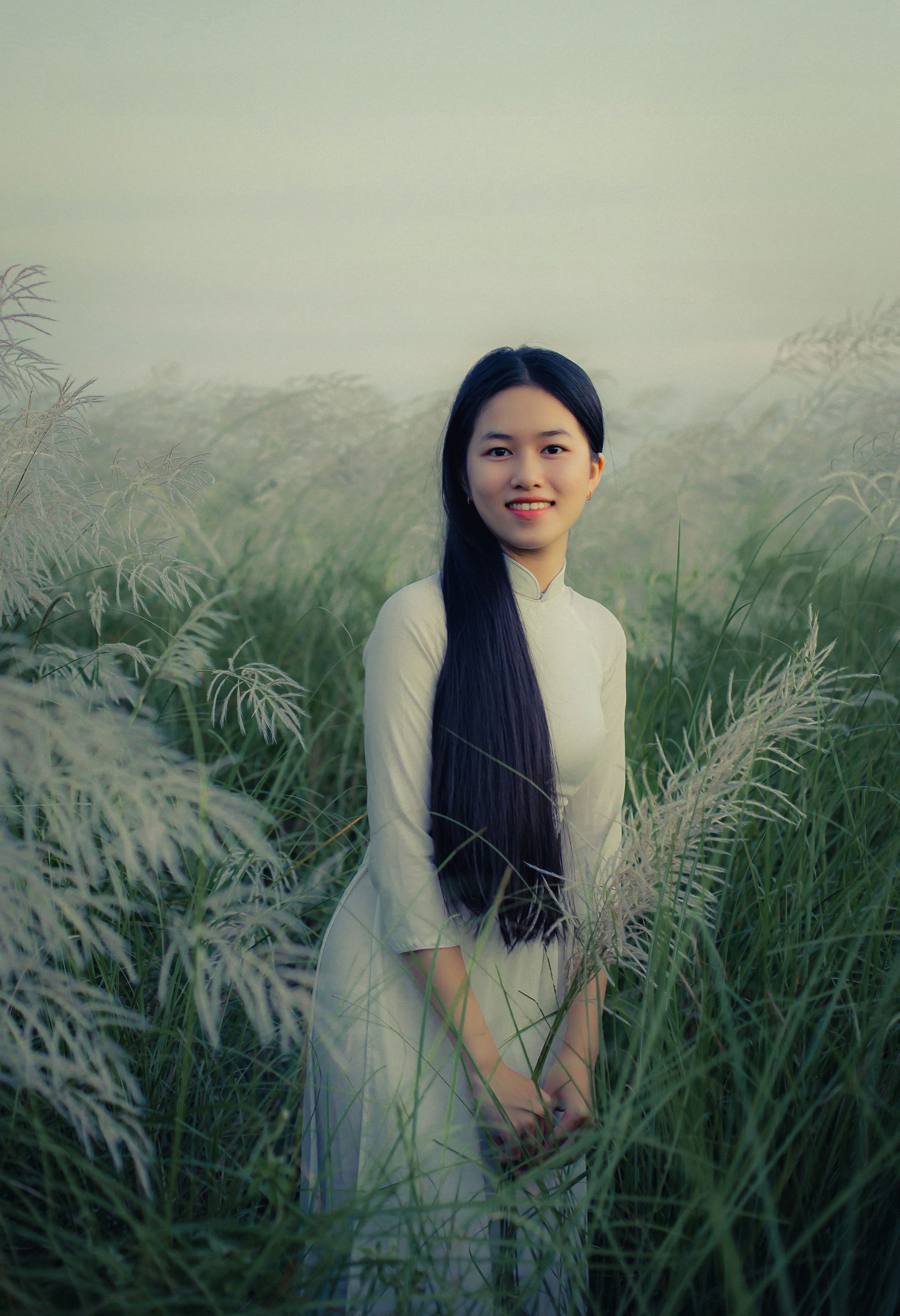 Woman wearing traditional áo dài standing in green field, Hội An, Vietnam.