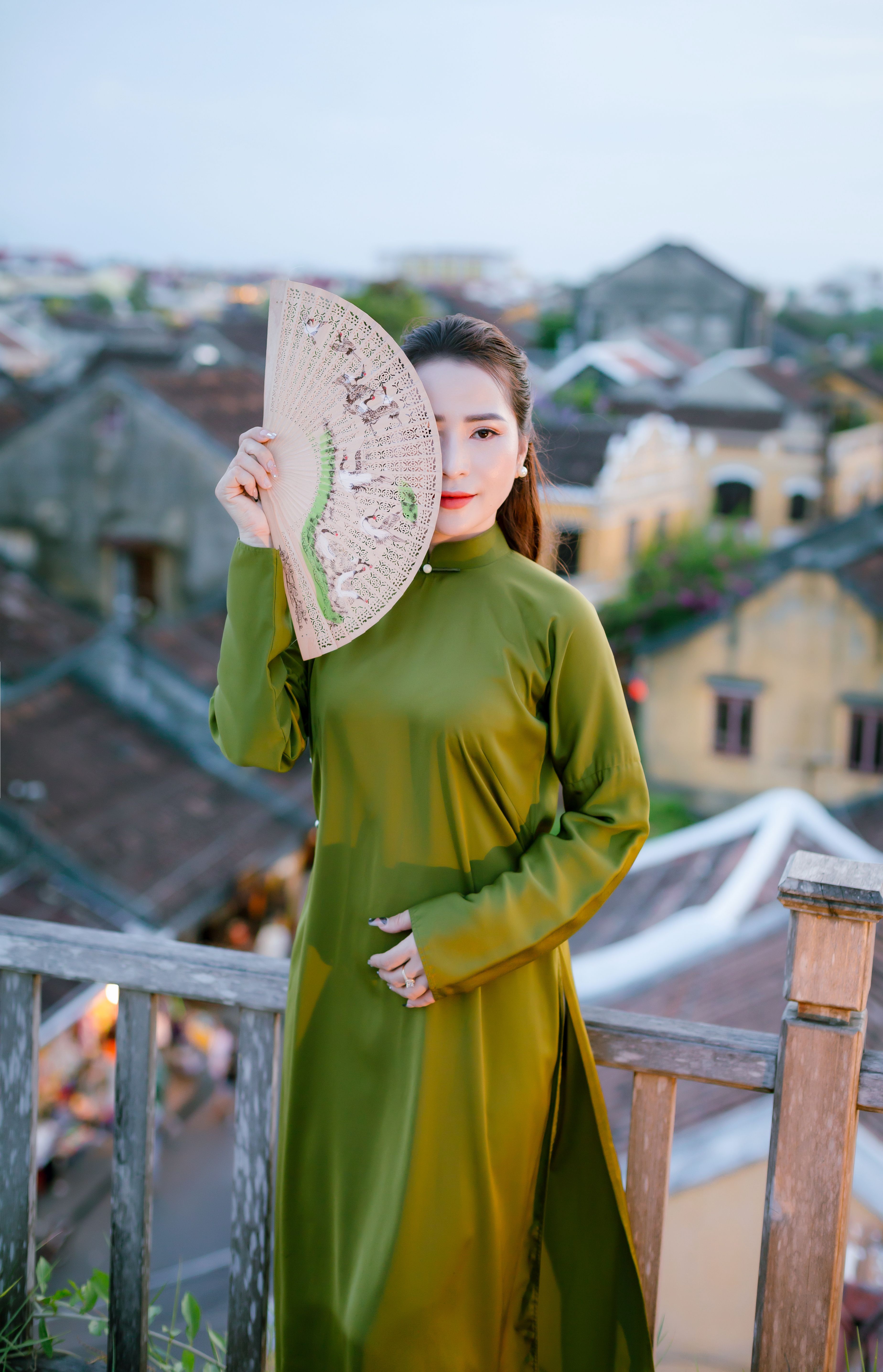 A woman in green traditional dress holds a fan in Hội An, Vietnam.