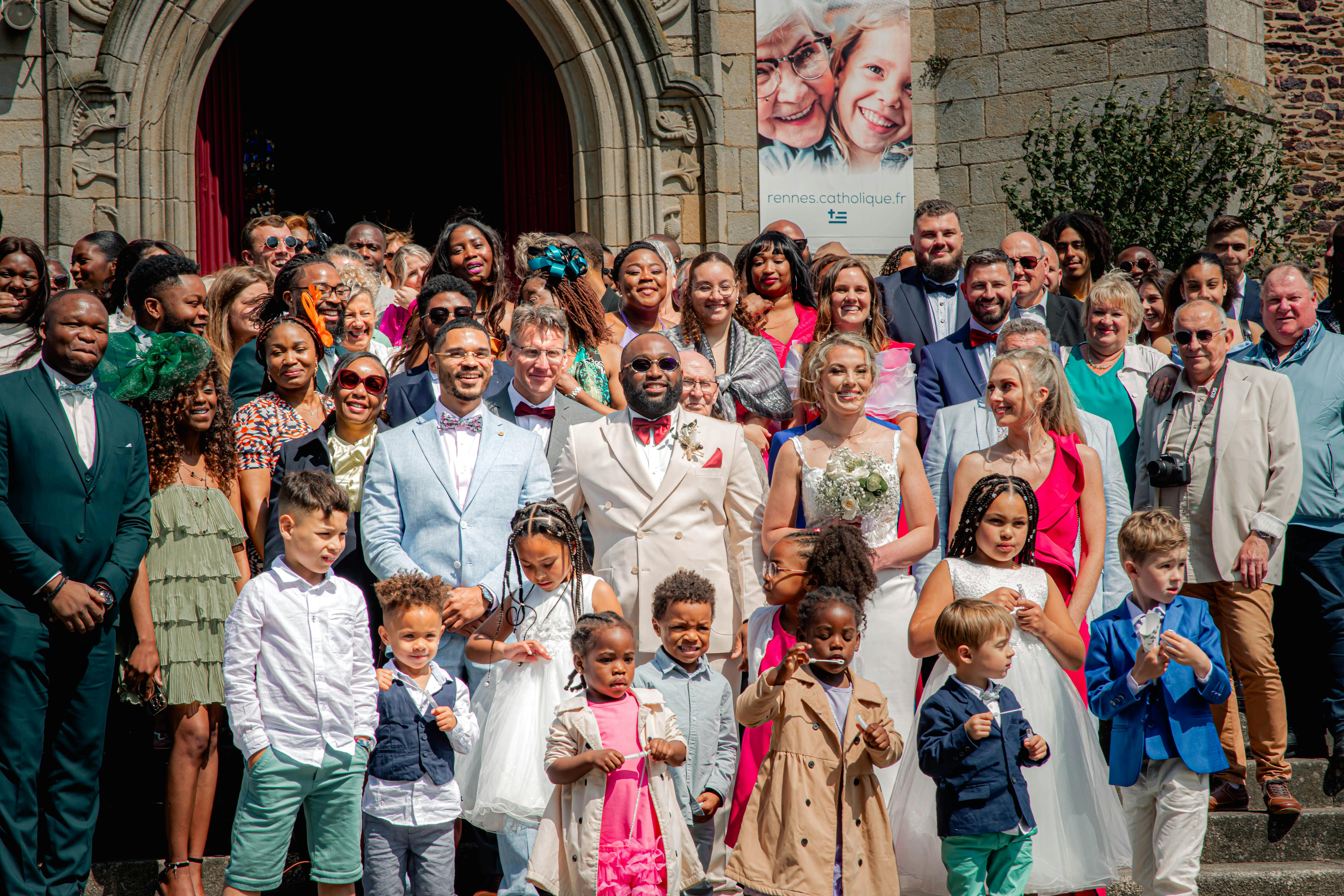 A large, joyful group gathered for a multicultural wedding outside a church.