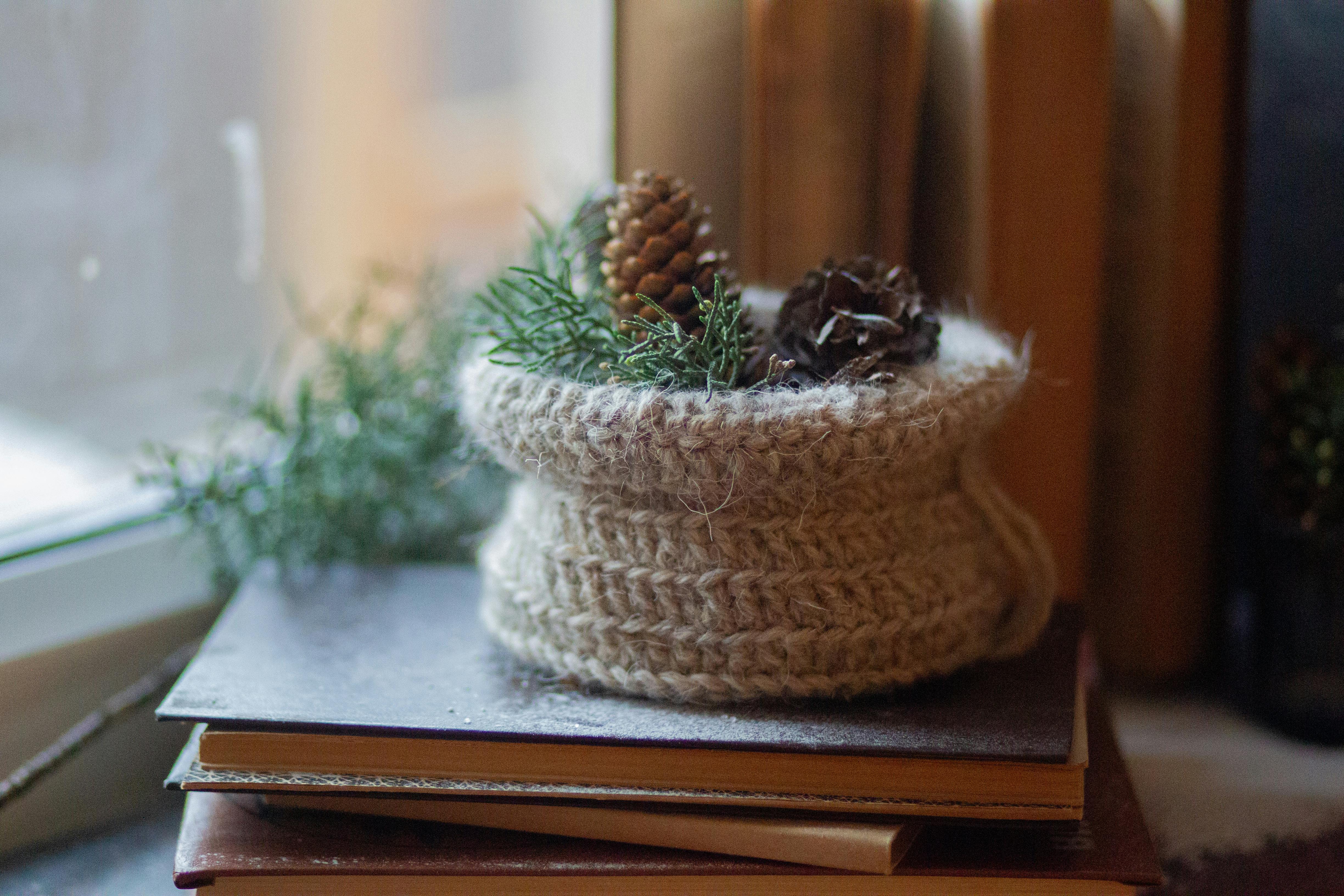 Free A knitted bag with pinecones sits atop books, creating cozy winter decor by a window. Stock Photo
