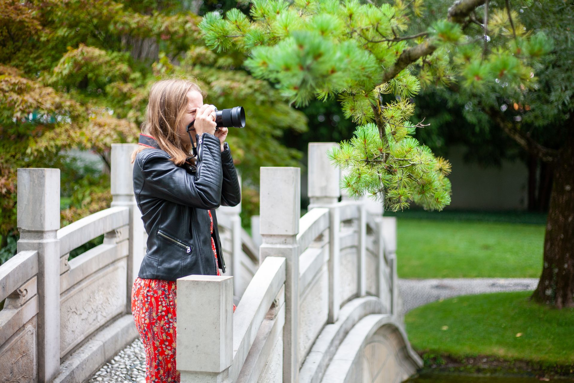 A woman taking photographs on a picturesque garden bridge surrounded by lush greenery.