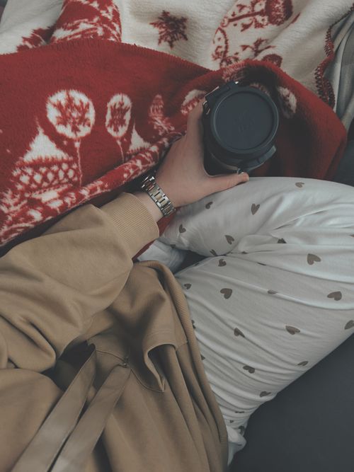 Free Relaxing indoors in heart-pattern pajamas with a warm drink and festive blanket. Stock Photo