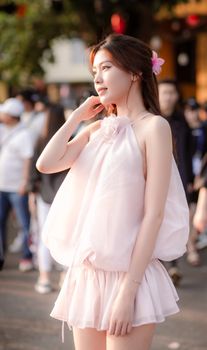 A young woman in a pink dress with flower in hair, posing outdoors in Hội An, Vietnam.