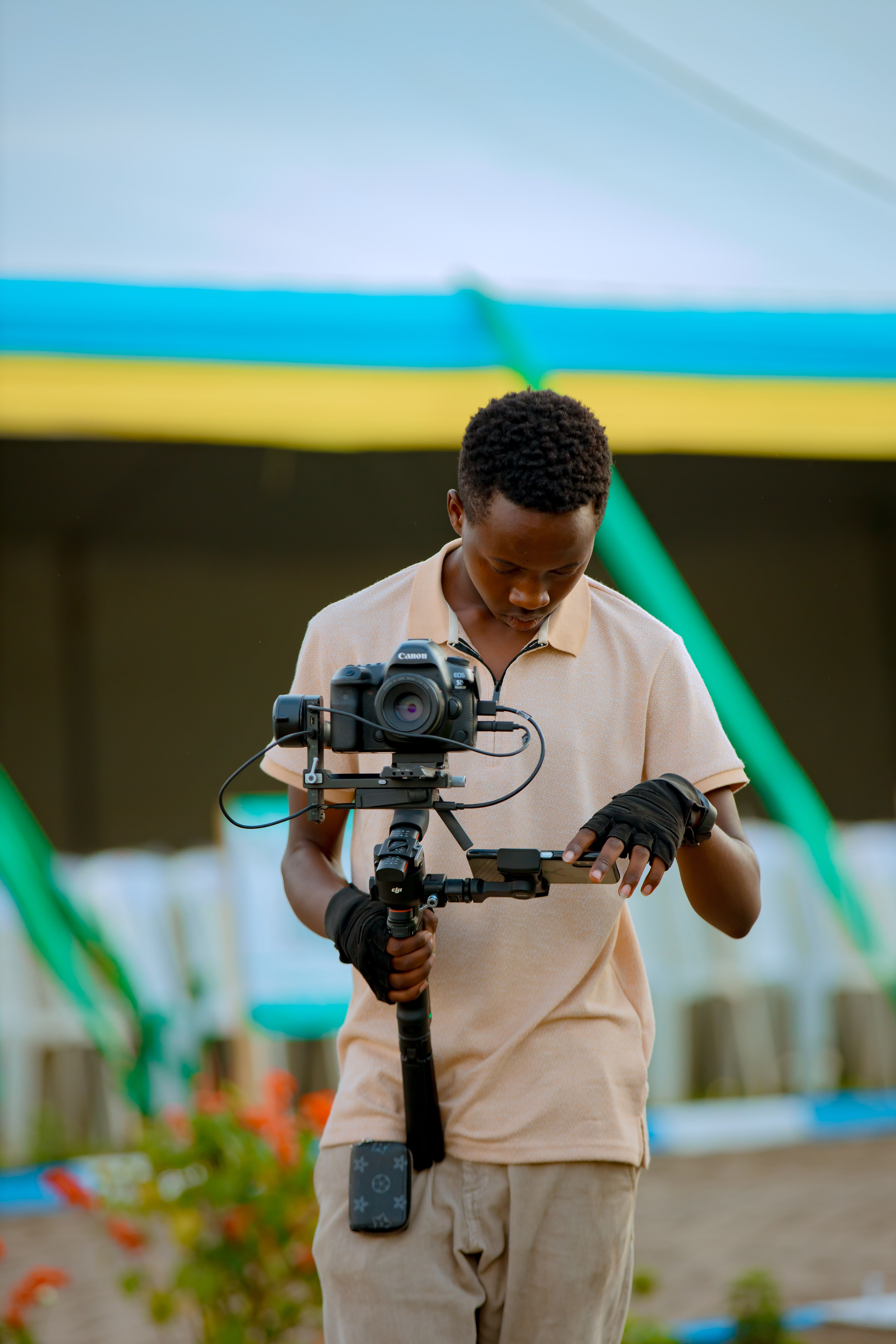 A young videographer fine-tuning gimbal settings outdoors. Bright and focused.