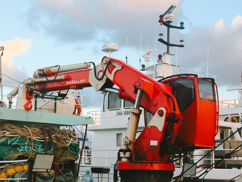 Red crane on an industrial fishing boat docked at the harbor with fishing nets