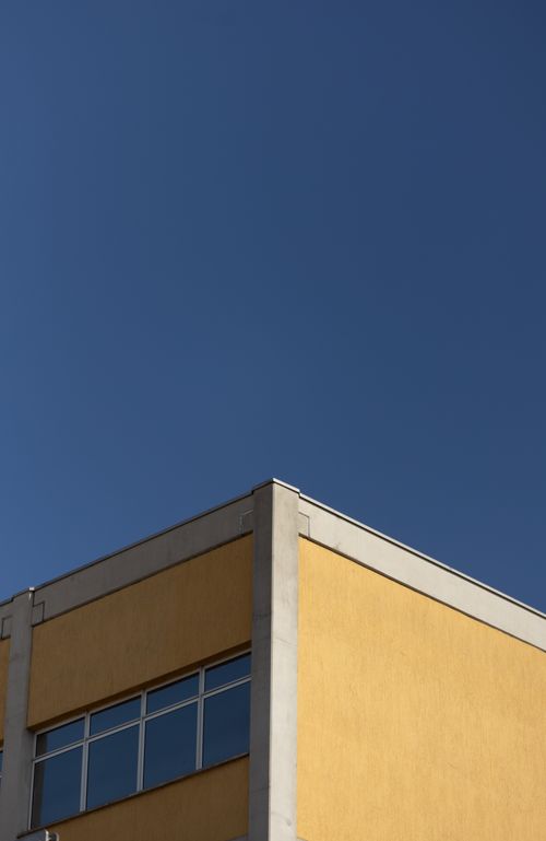 Free A minimalist architectural photo of a yellow building corner set against a clear blue sky. Stock Photo