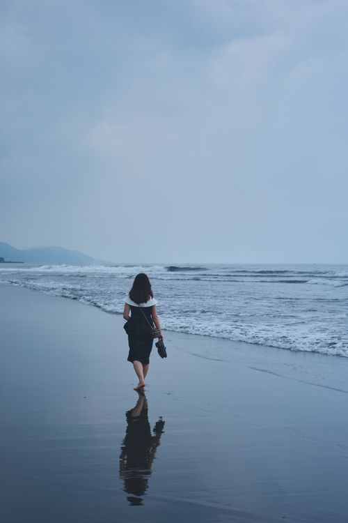 Free Solitary woman walking along a serene beach in Taiwan under a cloudy sky. Calm and peaceful scene. Stock Photo