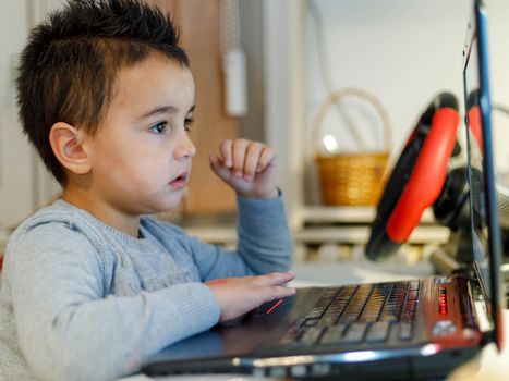 A young child focuses intensely on a laptop screen while learning from home, showcasing modern education.