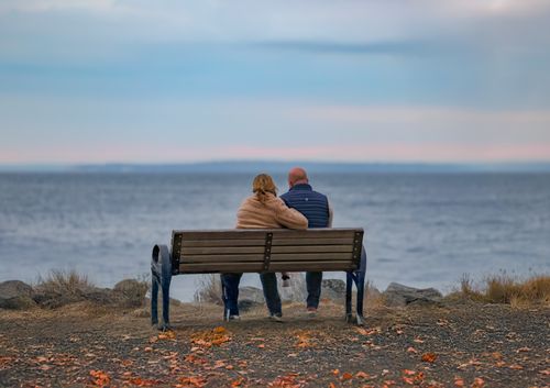 Free A couple sits on a bench, embracing the peaceful autumn scenery at Cove Island Park, Stamford. Stock Photo