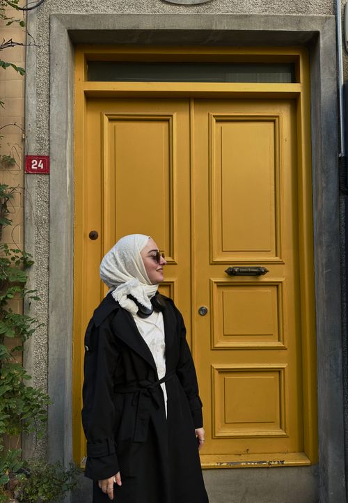 Free Woman in a headscarf stands confidently by a bright yellow door in İstanbul, Türkiye. Stock Photo