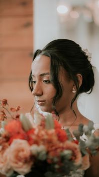Bride gazing at vibrant bouquet indoors, capturing elegance and beauty.