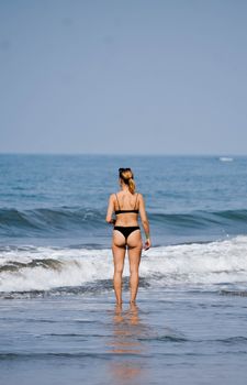A woman in a bikini stands facing the sea at Anjuna Beach, Goa, India.