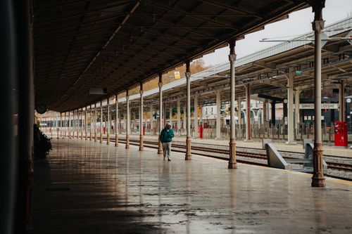Free A lone person stands on an empty urban train station platform under cloudy skies. Stock Photo