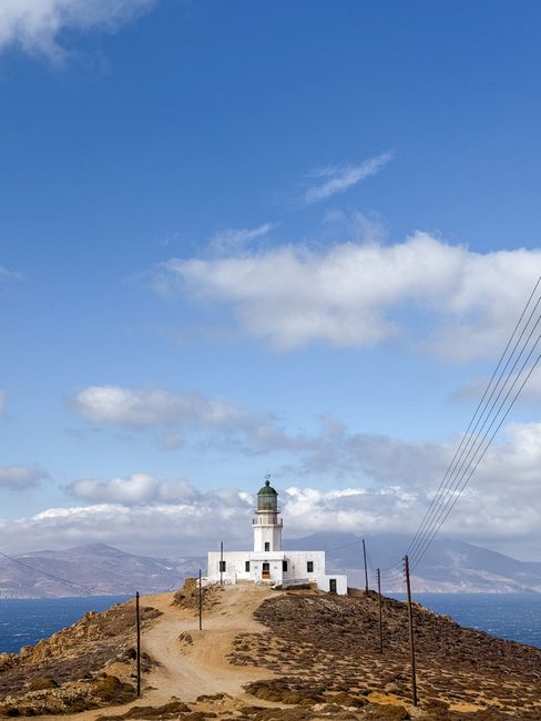 Scenic view of a solitary lighthouse perched on a Greek cliff with a vibrant sky.