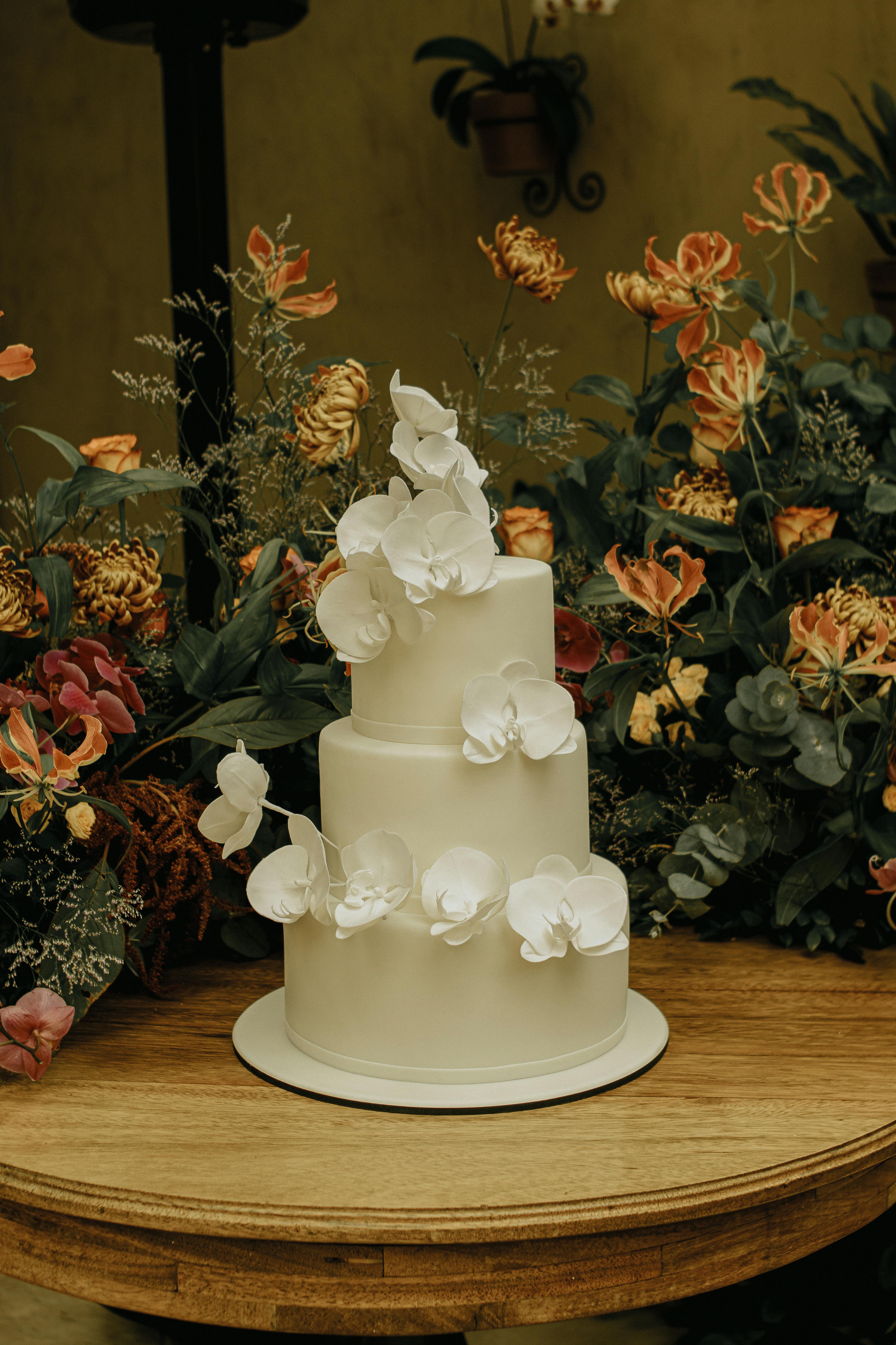 Elegant wedding cake decorated with white orchids and floral backdrop.
