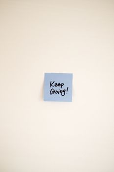 Blue post-it note with 'Keep Going!' message on a minimalist wall.