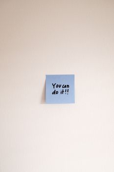 Blue Post-It note with 'You can do it!!' message on wall for encouragement.