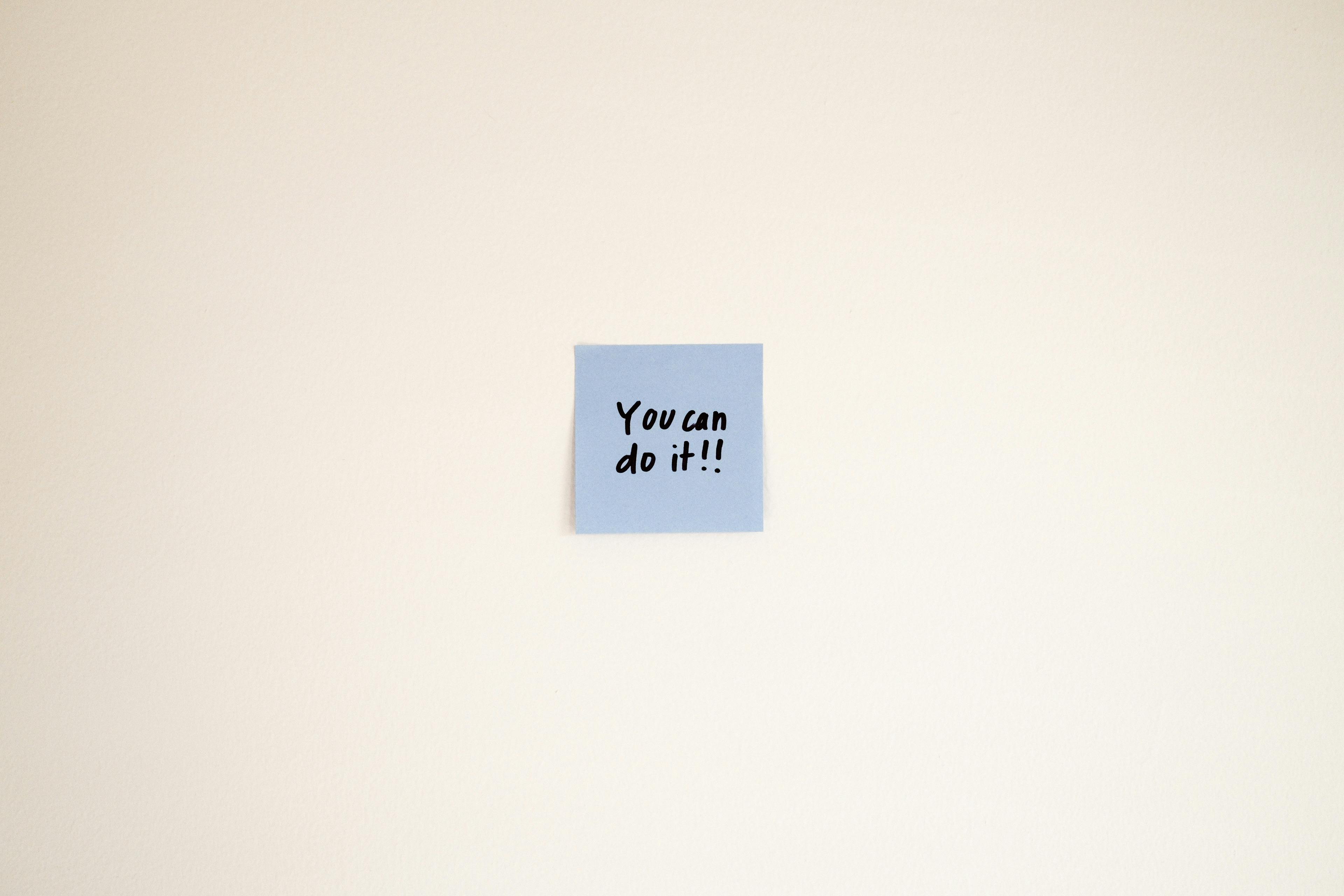 Gratis En motiverende besked på en blå Post-it seddel lyder "Du kan gøre det!" på en cremevæg. Lagerfoto