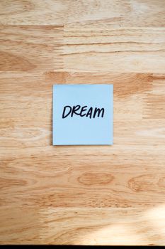A blue sticky note with the word 'DREAM' on a wooden surface, symbolizing motivation.