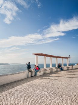 People enjoying a sunny day at a cliffside viewpoint in Nazaré, Portugal.