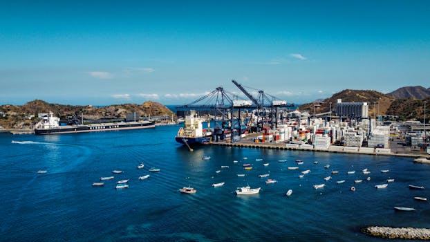 A busy port with cargo ships, containers, and boats under a clear blue sky.