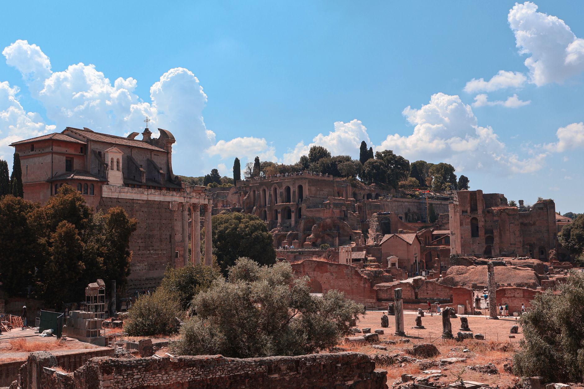 Explore ancient Roman ruins in Rome with clear skies, lush greenery, and historical architecture.