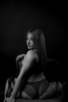 Artistic black and white photography of a woman in lingerie seated on a chair.