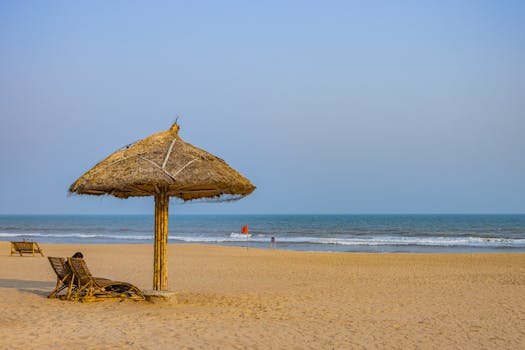 Calm beach scene in Puri, Odisha with a solitary straw umbrella by the ocean.