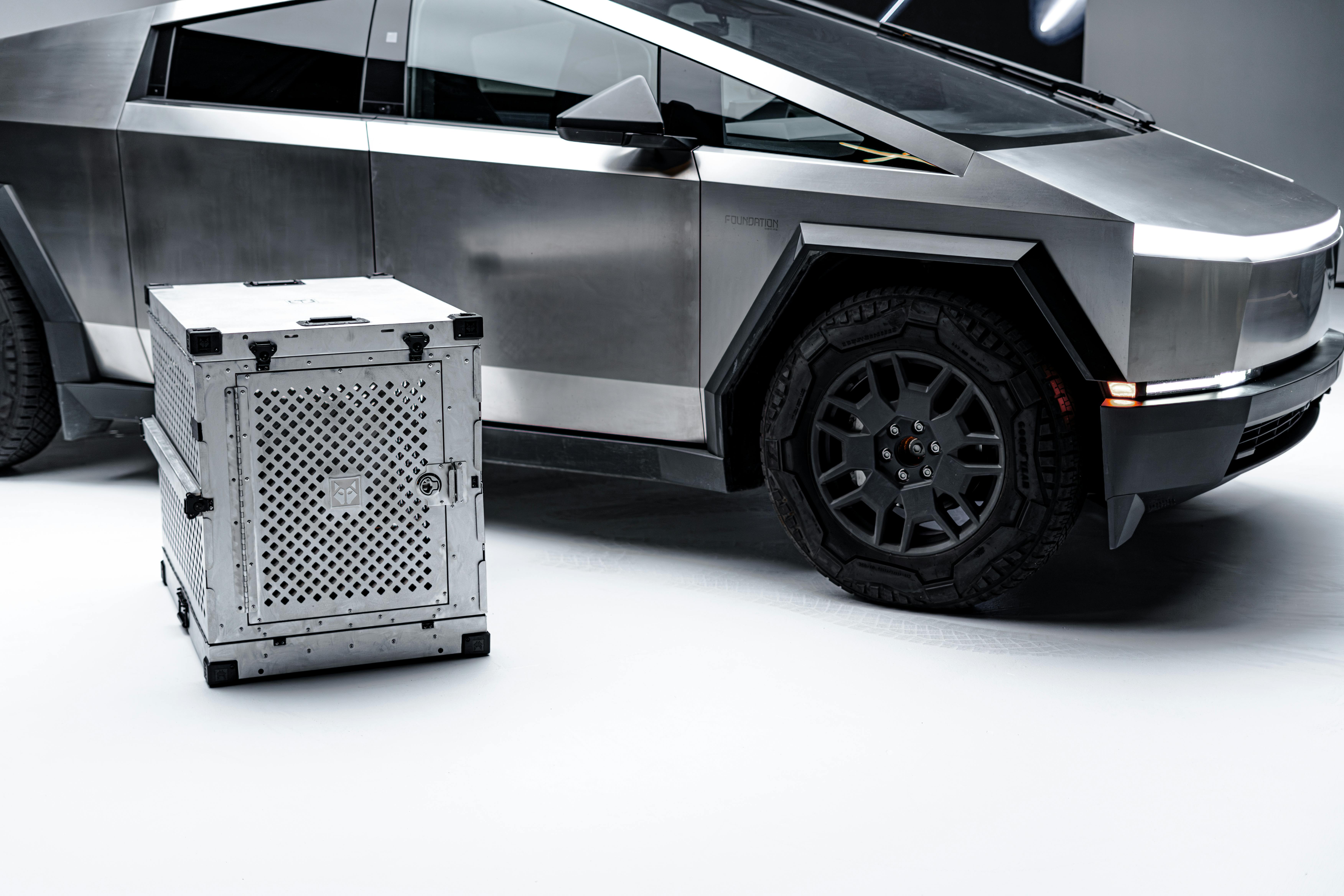 A sleek cybertruck beside a metallic, secure dog crate in a studio.