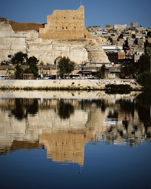 Free Historic fortress with cityscape reflecting in a tranquil river under clear blue skies. Stock Photo