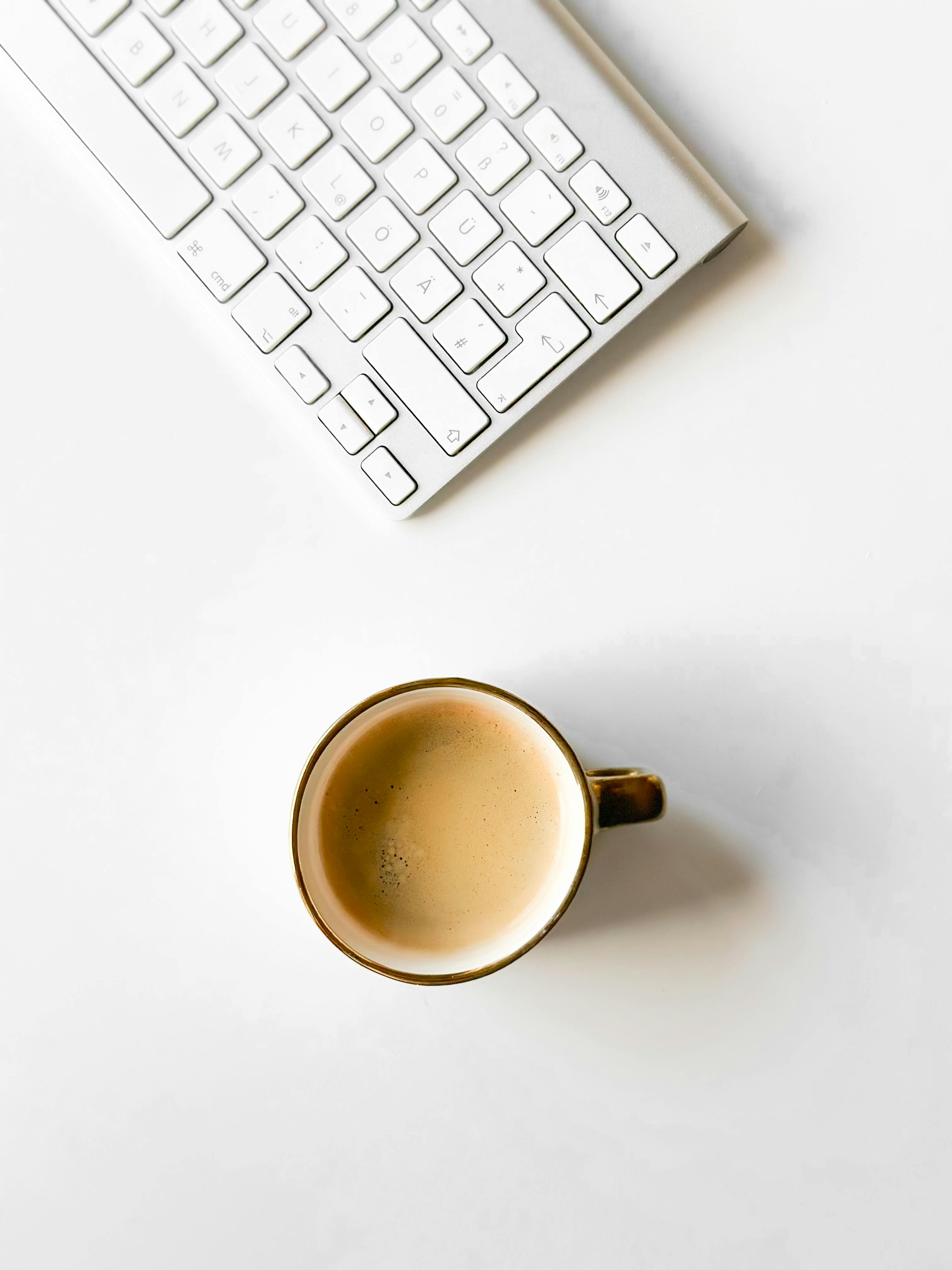 Top view of coffee mug and keyboard on a white desk, perfect for office themes.