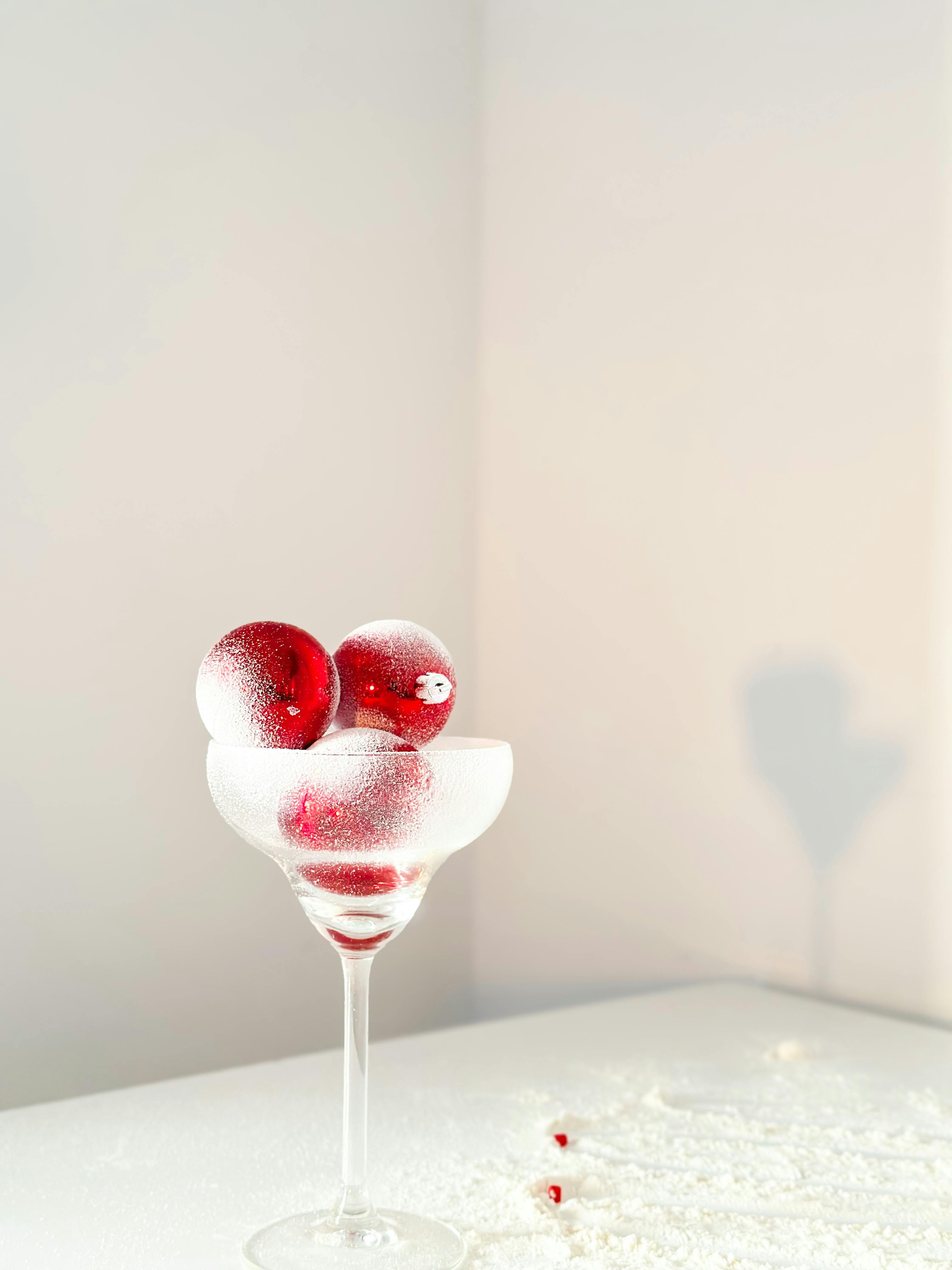 Elegant red Christmas baubles in a frosted martini glass, dusted with snow for holiday decor.