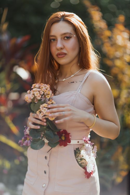 Free Beautiful young woman with flowers in a sunlit garden, exuding natural beauty and serenity. Stock Photo