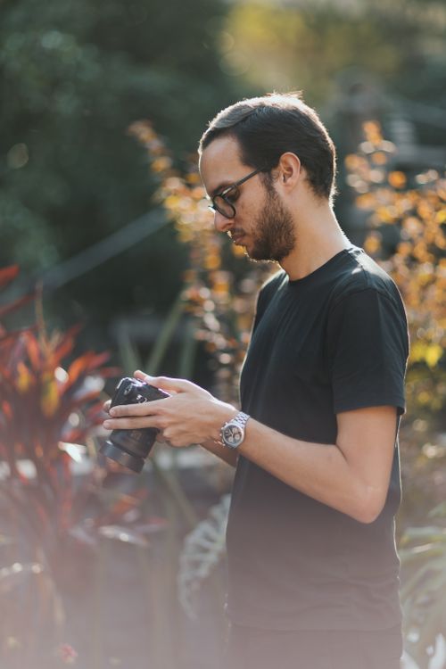 Free A male photographer reviews a photo on his camera in an outdoor garden setting. Stock Photo