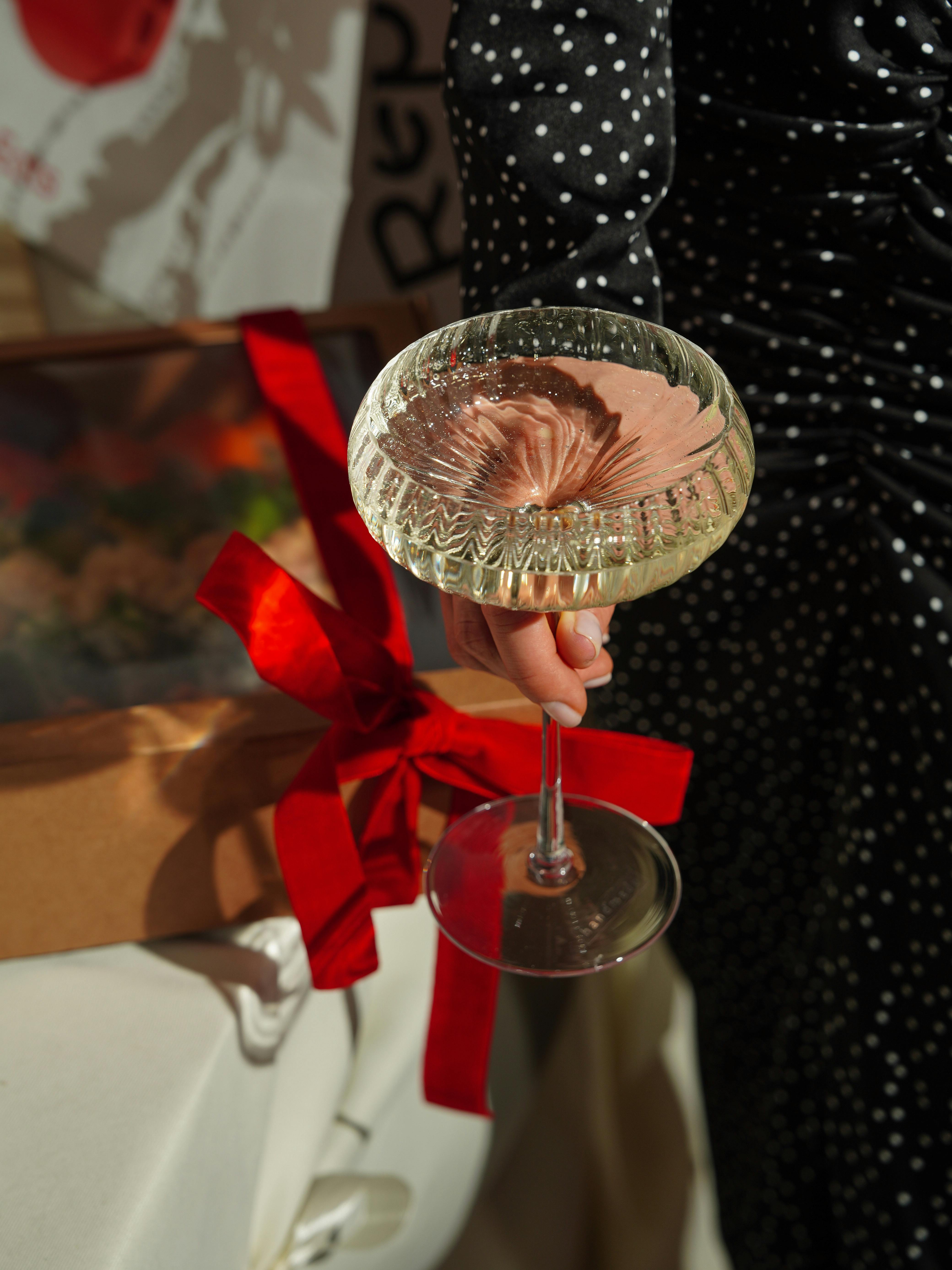 A woman holds a martini glass amidst a festive setup with gift box.