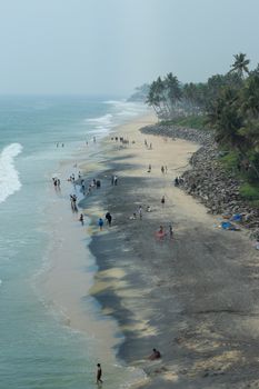Captivating Kerala beach scene with people enjoying the waves and palm-lined shore.