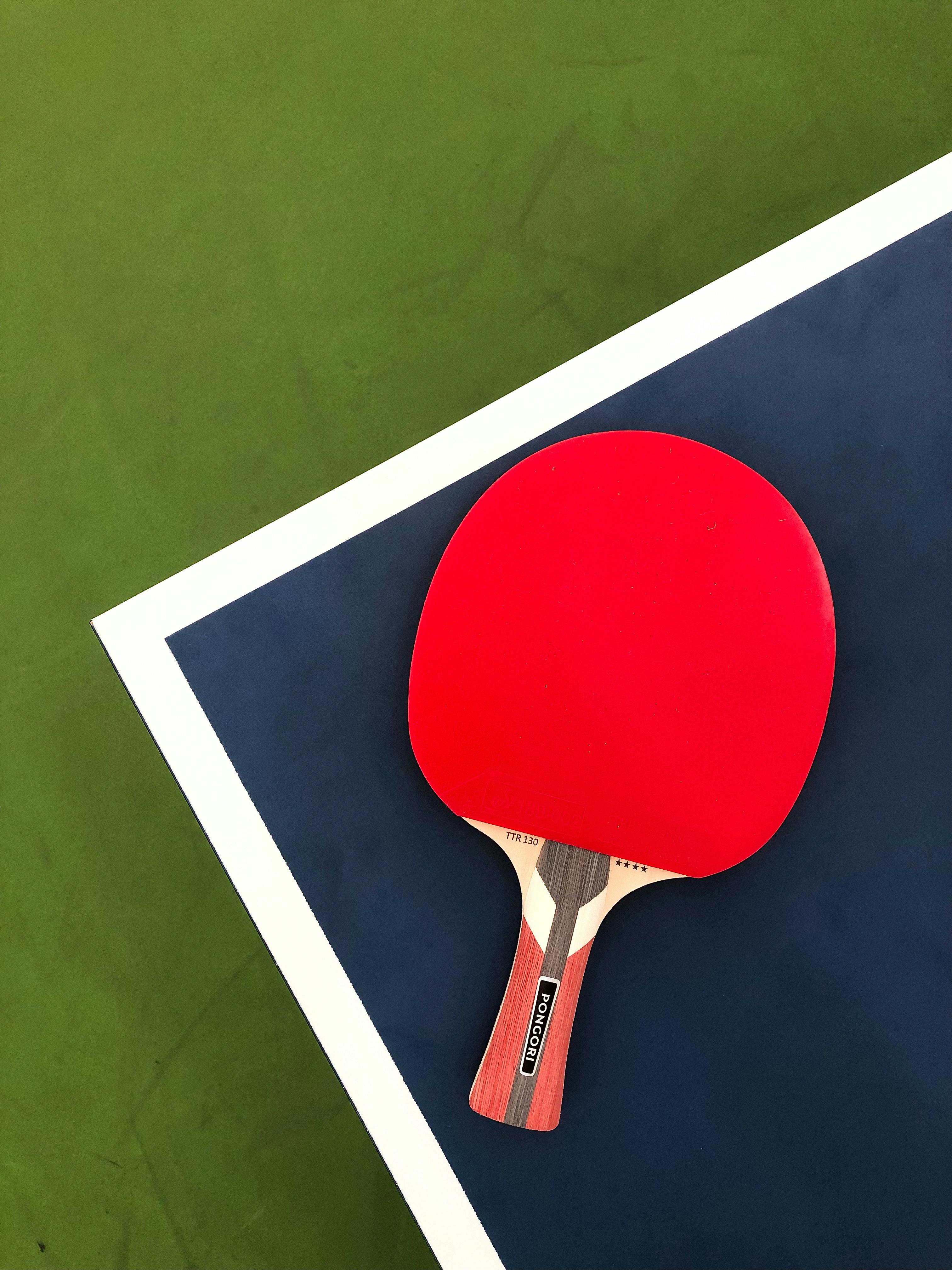 Red table tennis paddle on a green and blue table, perfect for sports enthusiasts.