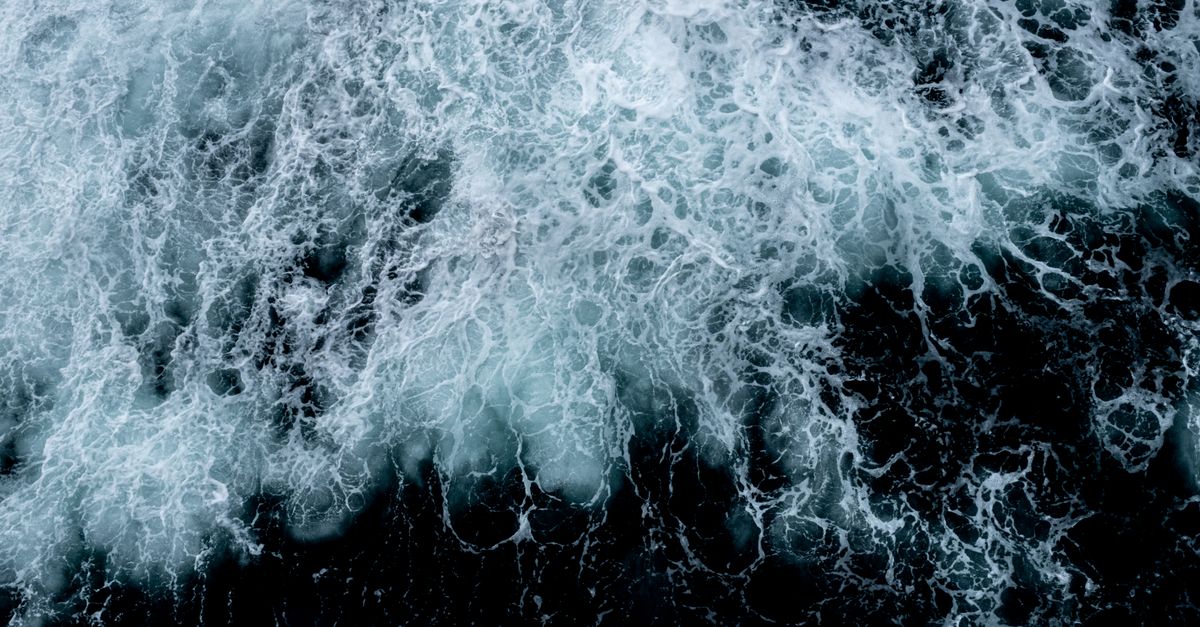 Vue dynamique de haut en bas des vagues écumeuses de l'océan créant des motifs abstraits.
