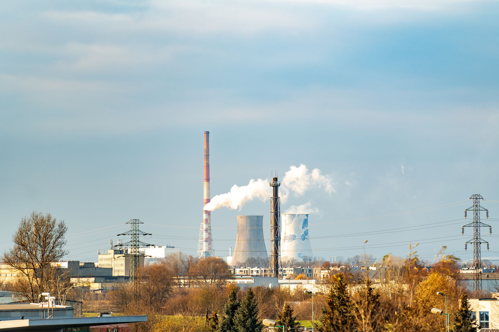 Distant view of an industrial power plant with cooling towers emitting smoke against a clear blue sky.