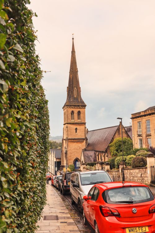 Free A scenic street view in Bath, England, featuring a historic church with parked cars and greenery. Stock Photo