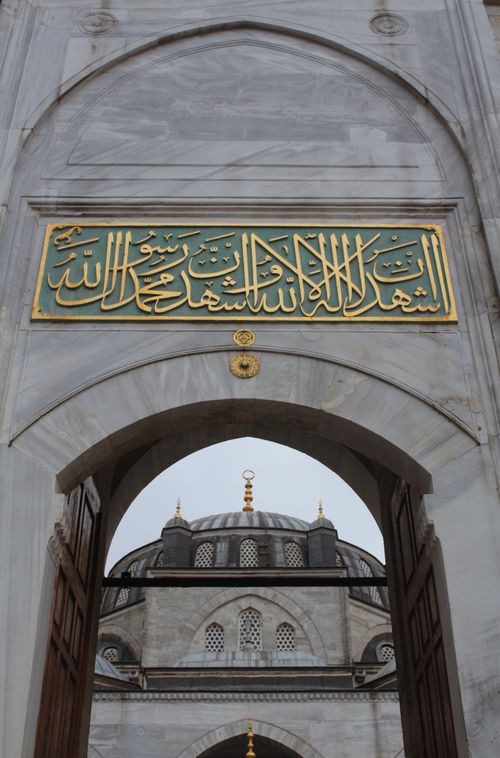 Free Marble archway with intricate Arabic calligraphy leading to a mosque dome. Stock Photo