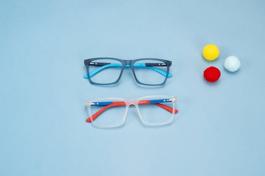 Colorful eyeglasses displayed on a subtle blue backdrop with decorative pom-poms, capturing modern eyewear fashion.