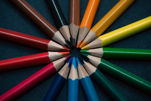 A vivid display of multicolored pencils arranged in a circular pattern on a dark background.
