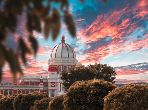 Free Elegant dome architecture captured against a breathtaking sunset sky, flanked by lush greenery. Stock Photo