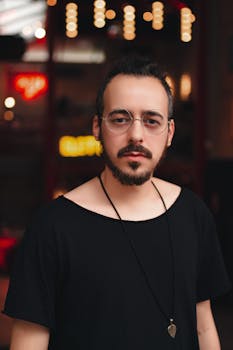 一幅肖像画中，一位留着胡须、戴着眼镜、衣着时尚的男子，置身于光线昏暗的室内空间