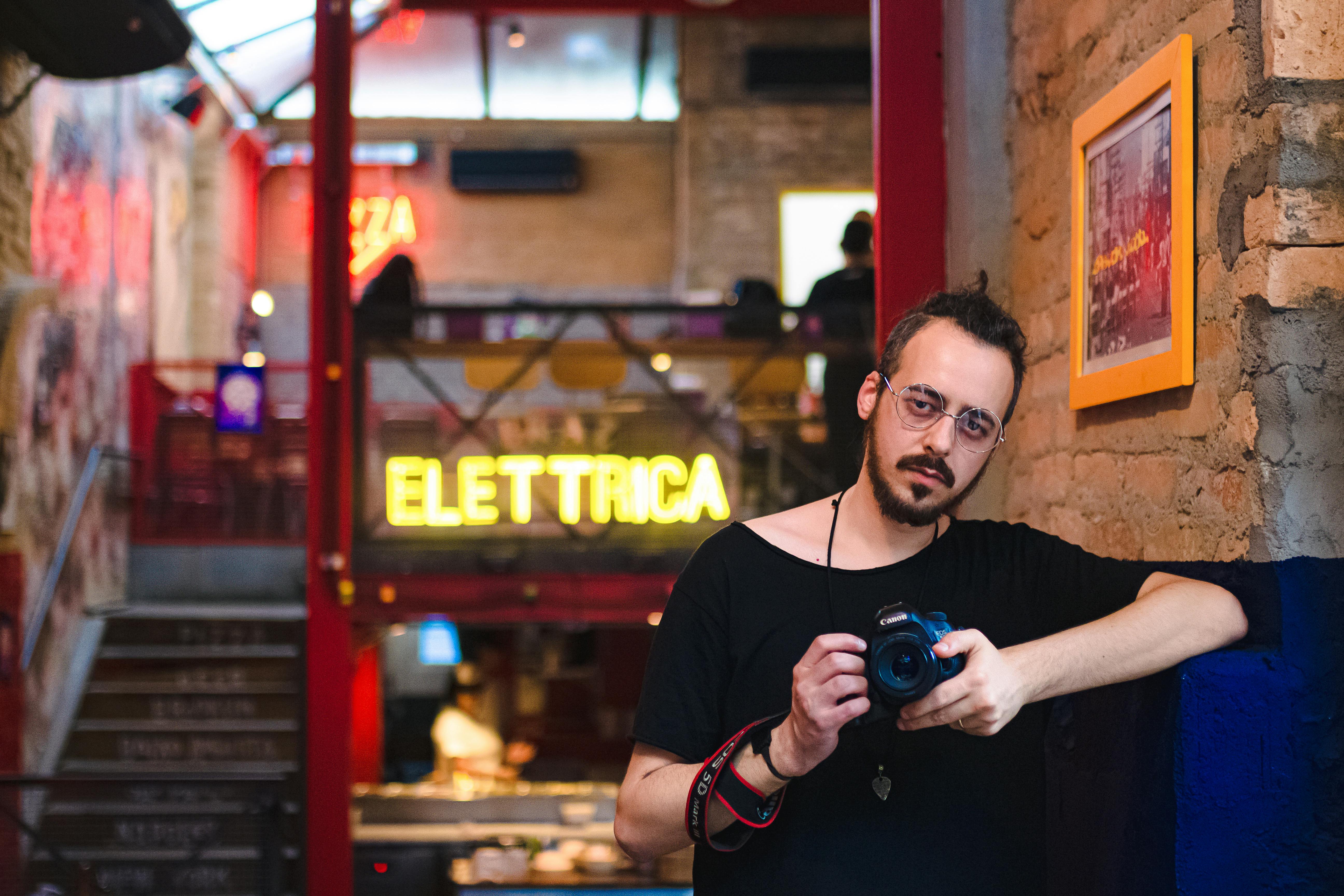 man wearing black scoop neck shirt holding black canon dslr camera