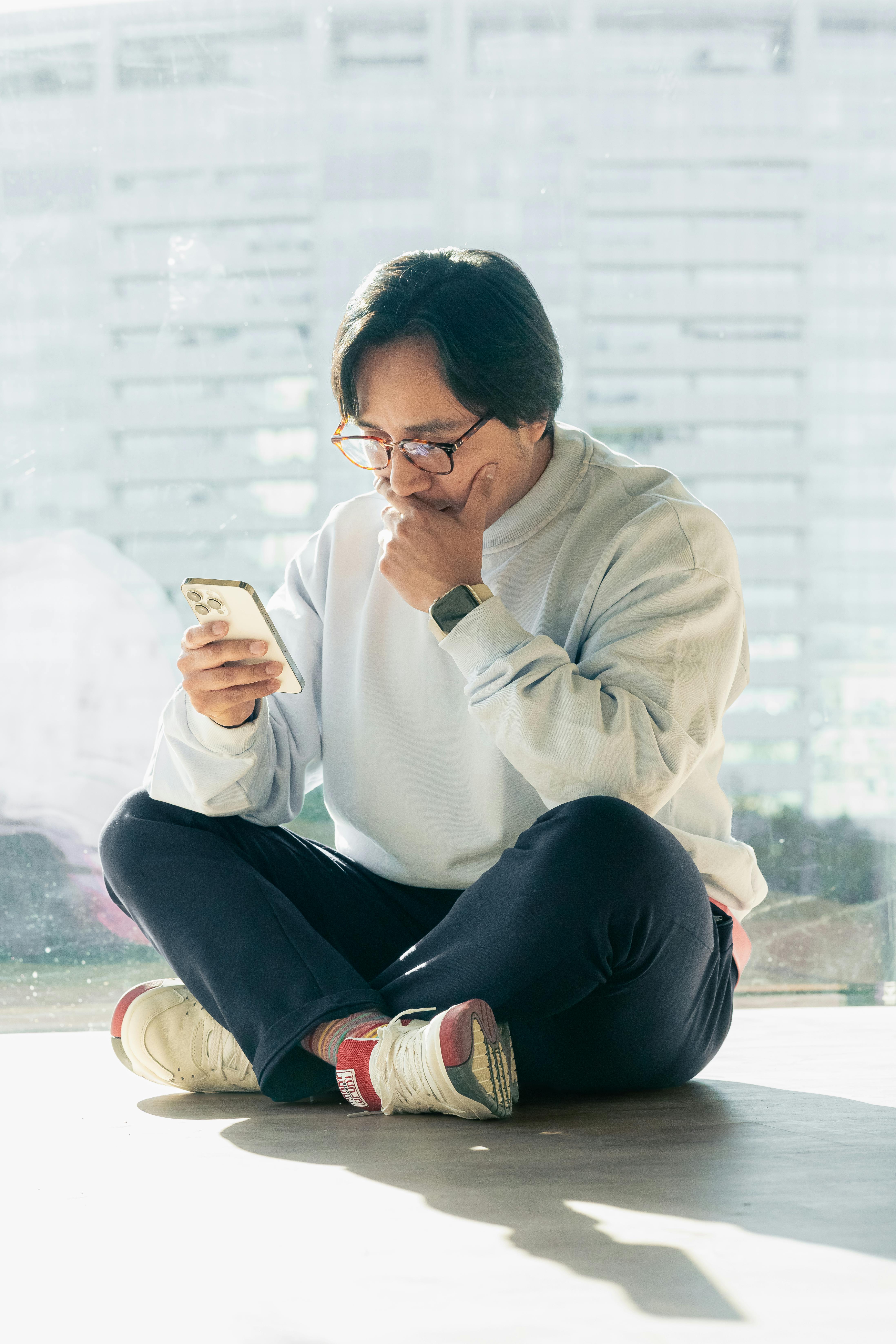 Man in casual attire sitting indoors, using smartphone against city backdrop.