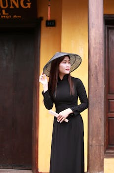 Elegant woman in black áo dài dress with hat in Hội An, Vietnam.