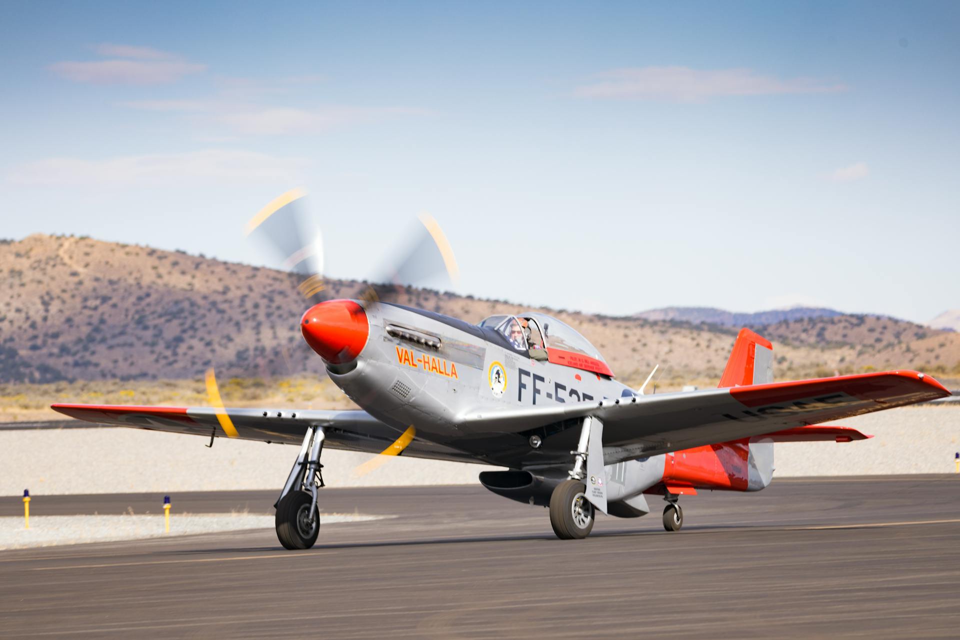 Classic P-51 Mustang aircraft with spinning propellers on a runway against a scenic mountain backdrop.