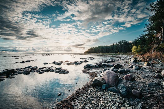 Capture of a serene sunrise over a rocky beach, with reflections on calm waters.